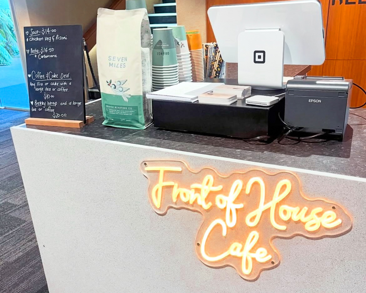 Front of House Cafe counter with neon sign and coffee bar setup